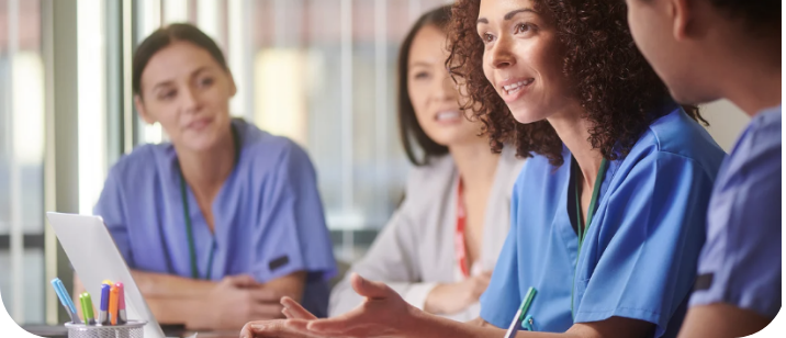 Healthcare professionals in discussion around a table with a laptop.