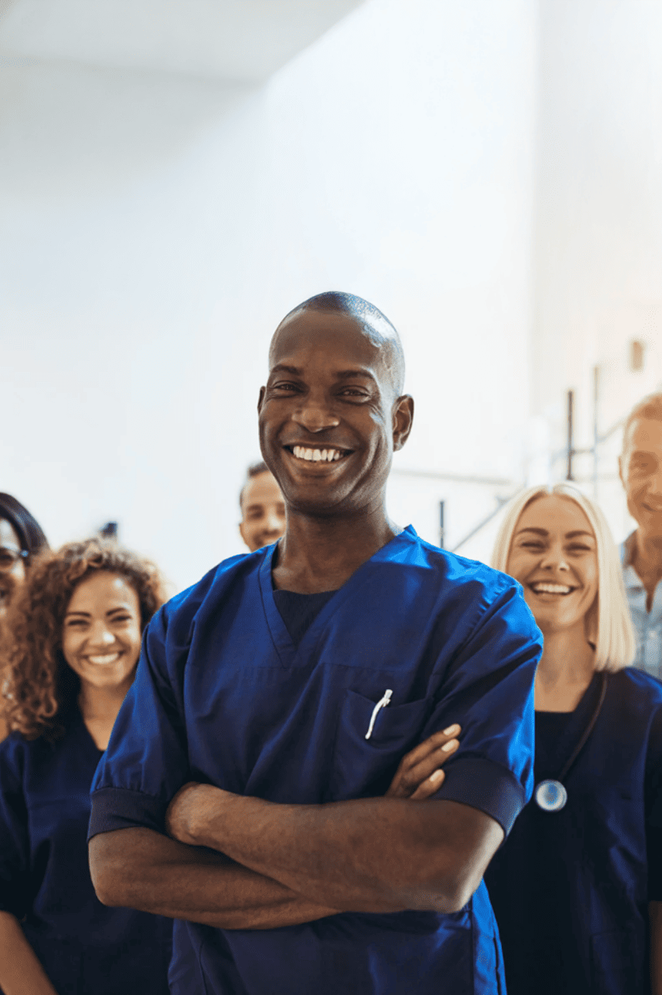 Smiling healthcare team in blue scrubs, led by man with arms crossed.